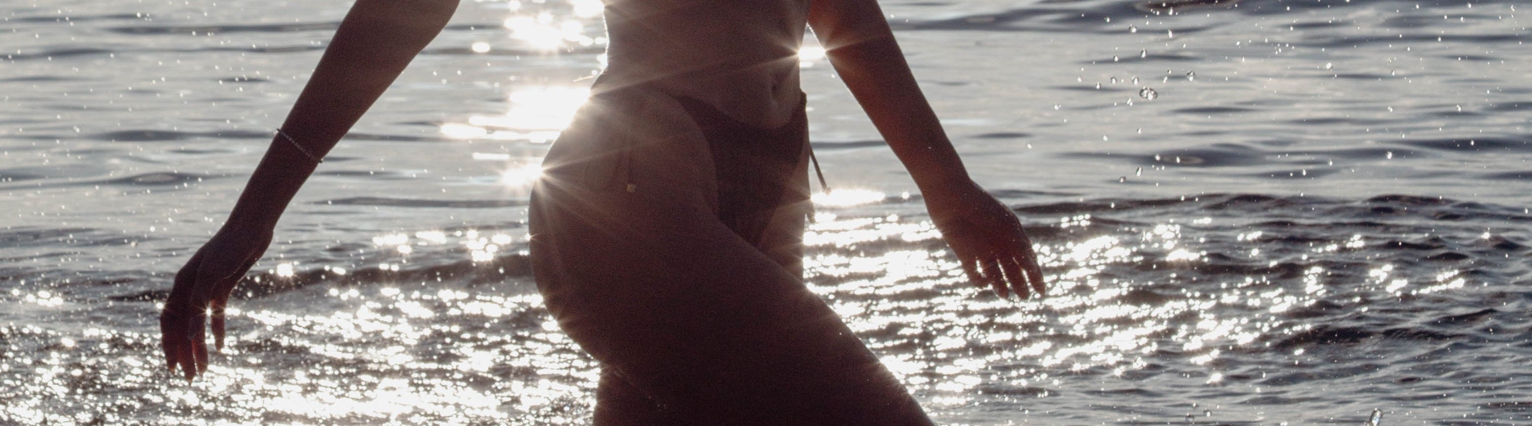 Woman in a bikini standing in shallow water at sunset